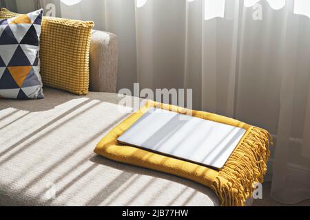 Closed laptop on sofa in cozy living room interior. Take a break. Time to rest. Time for vacation. Work from home Stock Photo