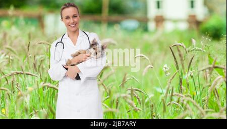 Image of happy caucasian female vet holding yorkshire terrier pet dog, over grasses in garden Stock Photo