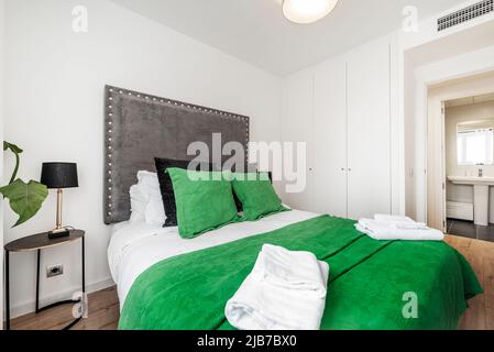 Bedroom with a double bed dressed in a striking green bedspread and matching cushions Stock Photo
