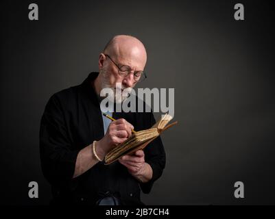 Head and shoulders portrait of bald and bearded senior man in kimono writing a journal Stock Photo