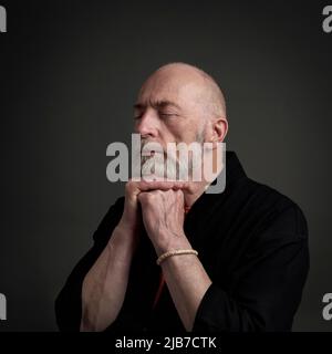 Head and shoulders portrait of bald and bearded senior man with closed eyes contemplating, meditating or praying Stock Photo