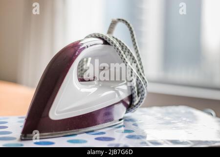 Electric cloth iron on ironing board in room Stock Photo