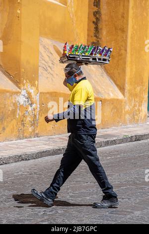 A man walking across the street carrying a tray of chips. San Miguel de Allende, Mexico. Stock Photo