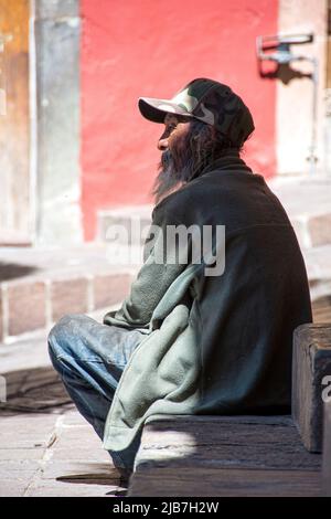 A Mexican man of Asian descent sits next to a fountain in one of Guanajuato, Mexico's numerous plazas, people watching.in Stock Photo