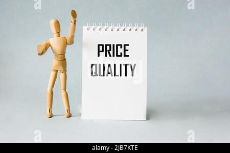 Text about quality and price on a notebook, next to a wooden doll. Low price and high quality service Stock Photo