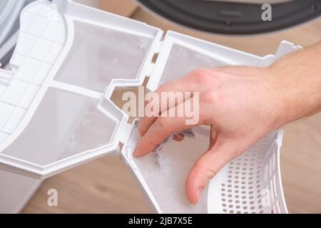A man takes a lint filter out of the dryer and cleans it from dust, lint, hair, wool. Stock Photo