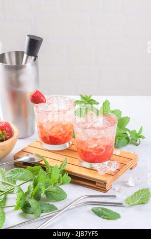 Cold strawberry cocktail mojito, margarita, daiquiri in two glasses with mint, ice and bartender tools on light table Stock Photo