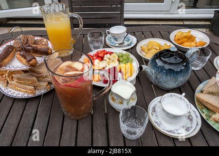The Queen's Platinum Jubilee bank holiday - table set for a family afternoon tea in the garden with sandwiches, cakes, tea, juice and fruit, June 2022 Stock Photo