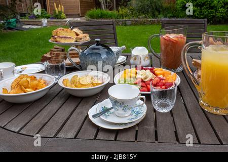 The Queen's Platinum Jubilee bank holiday - table set for a family afternoon tea in the garden with sandwiches, cakes, tea, juice and fruit, June 2022 Stock Photo