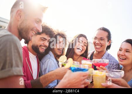 Friends cheers and having fun drink color cocktails in a rooftop bar. We are so lucky to have each other. Stock Photo