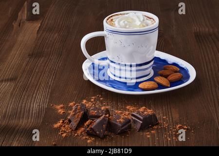 Cup of coffee with whipped cream and almonds, chopped chocolate on a brown wooden table. Coffee based drinks Coffee day Stock Photo
