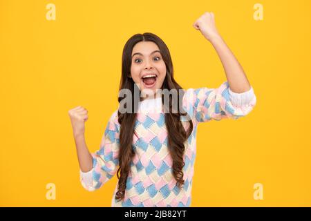 Excited face. Amazed expression, cheerful and glad. Teenager child overjoyed successful do winner gesture clench fist say yes isolated on yellow Stock Photo