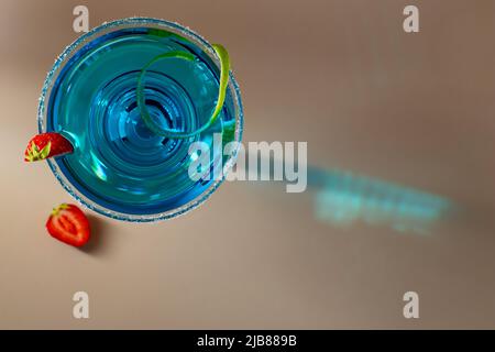 Glass with blue margarita cocktail garnished with lime zest and strawberries Stock Photo