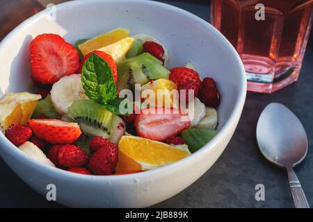 Fruit salad in a white bowl on a tray with a drink and a spoon Stock Photo