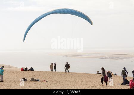 Picture of tourists on Dune du Pilat in front of a paraglider in Arcachon Bay, France. The Dune of Pilat also called Grande Dune du Pilat, is the tall Stock Photo