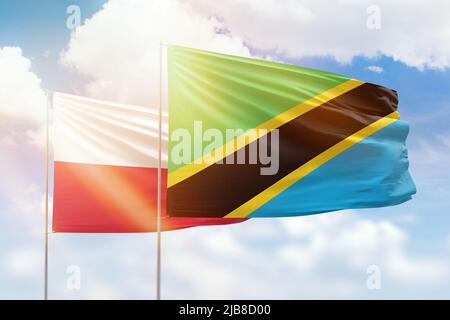 Tanzania and Poland flags waving together in the wind on blue cloudy ...
