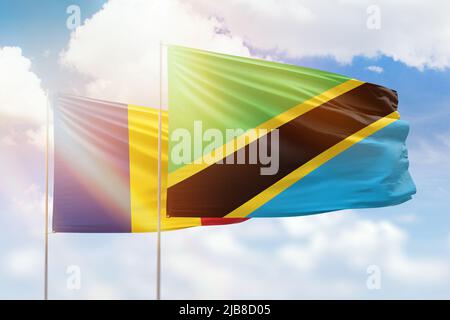 Tanzania and Romania flags waving together in the wind on blue cloudy ...