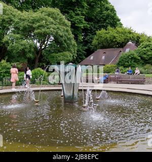 London, Greater London, England, May 28 2022: People enjoying a sunny spring day beside the fountain and cottage at Holland Park in the Kensington are Stock Photo