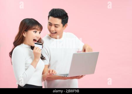 Excited young couple shopping online, holding credit card and looking at laptop Stock Photo