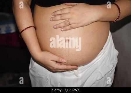young pregnant women showing her round belly womb with hand from different angle Stock Photo