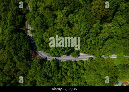 Winding road is meandering between blue sea and green mountains. Aerial view of car driving along the winding mountain road in Sochi, Russia. Stock Photo