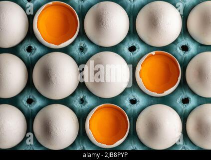 Organic fresh chicken eggs arranged in egg tray. half broken egg with yolk visible Stock Photo