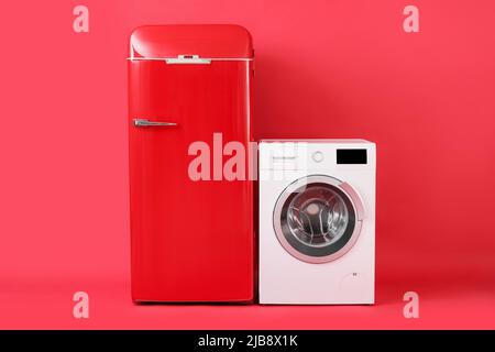 Stylish retro fridge and washing machine on red background Stock Photo