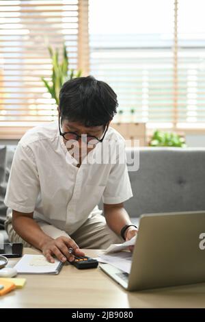 Focused man using laptop computer and calculating household expenses. Household finances concept. Stock Photo