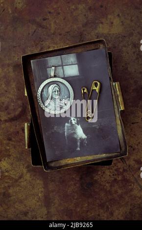 Vintage brass box containing 1950s photo of dog beneath window and brass safety pins and silver pendant of Virgin Mary Stock Photo