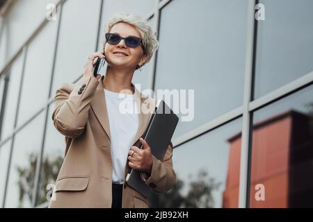 Modern Business Lady Smile and Talking on the Phone When Holding Laptop Outdoors Stock Photo