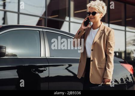 Elegant Business Woman with Briefcase in Hand Talking on the Phone Near the Luxury Car Stock Photo