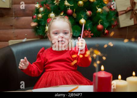 A little girl with a pencil in her hand looks lit firework sparkler. Stock Photo