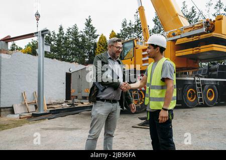 Foreman and customer or client agree about future building work on construction site. Man looking in paper, architect discussing project with builder Stock Photo
