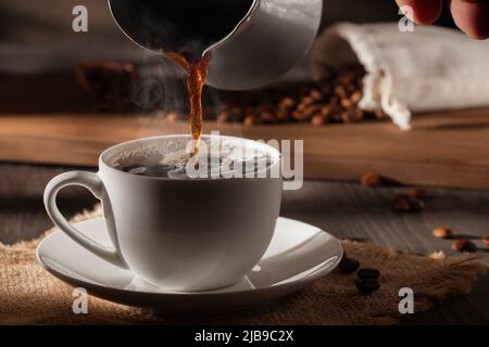 Pouring freshly brewed hot cezve coffee into a white cup. Stock Photo