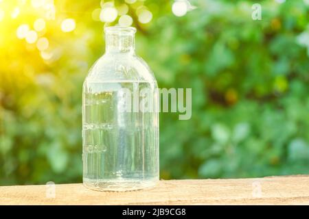 Clean water in a transparent glass bottle on a wooden table against the background of a green park in the rays of bright sunlight. environmentally fri Stock Photo