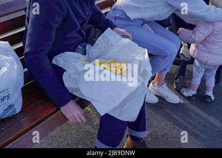 man with fish and chips on his lap in a coastal town in Britain Stock Photo