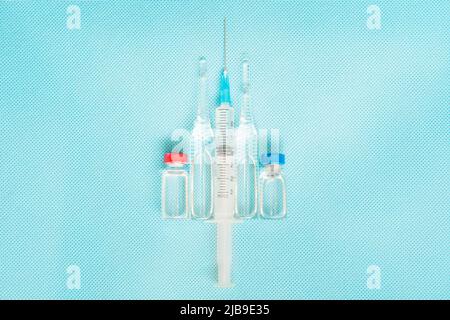 Syringe in the center of scene and red and blue ampoules with vaccine against virus situated vertical on blue background. Copy space. Stock Photo