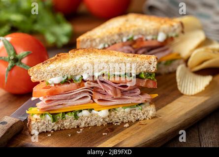 Ham sandwich with cheese, lettuce and tomato on whole grain bread.  Lettuce and tomatoes in background Stock Photo