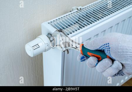 turning down thermostat on radiator to save energy due to heating cost price hike. Saving natural gas and energy efficiency at home. saving energy in Stock Photo