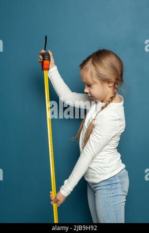 Little child girl holding measuring tape on blue background Stock Photo