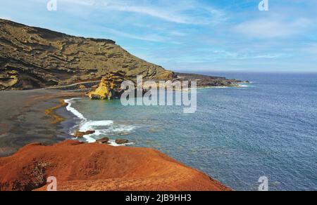 Beautiful secluded lagoon surrounded by impressive rugged weathered cliffs, different colors,red rock,  empty deserted black sand beach - El Golfo, La Stock Photo