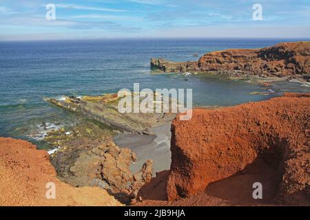 Beautiful secluded lagoon surrounded by impressive rugged weathered cliffs, different colors,red rock,  empty deserted black sand beach - El Golfo, La Stock Photo