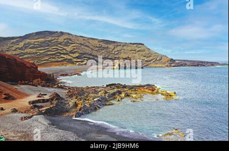 Beautiful secluded lagoon surrounded by impressive rugged weathered cliffs, different colors,red rock,  empty deserted black sand beach - El Golfo, La Stock Photo