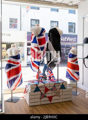 Colourful shop window display commemorating the Platinum Jubilee of Queen Elizabeth. Bright union flags draped on mannequins beside St Pirrans B&W Stock Photo