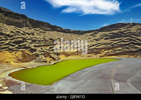 Beautiful secluded lagoon valley, red rocks, deep green lake (Lago verde), black lava sand, impressive rugged sharp steep cliffs - El Golfo, Lanzarote Stock Photo