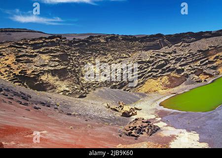 Beautiful secluded lagoon valley, red rocks, deep green lake (Lago verde), black lava sand, impressive rugged sharp steep cliffs - El Golfo, Lanzarote Stock Photo