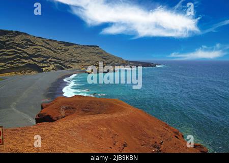 Beautiful secluded lagoon surrounded by impressive rugged weathered cliffs, different colors,red rock,  empty deserted black sand beach - El Golfo, La Stock Photo