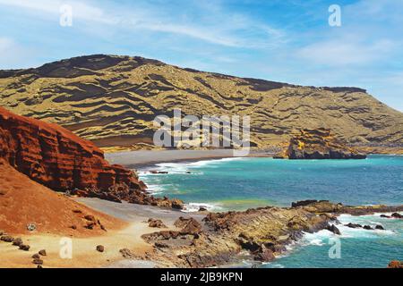 Beautiful secluded lagoon surrounded by impressive rugged weathered cliffs, different colors,red rock,  empty deserted black sand beach - El Golfo, La Stock Photo