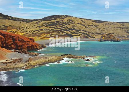 Beautiful secluded lagoon surrounded by impressive rugged weathered cliffs, different colors,red rock,  empty deserted black sand beach - El Golfo, La Stock Photo