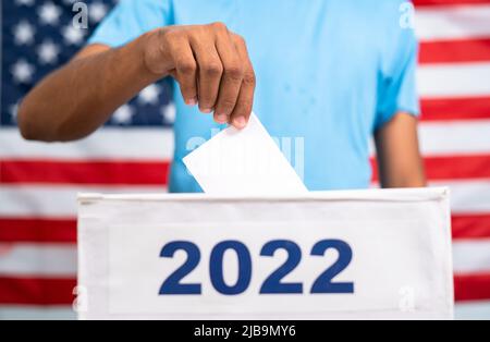 Man placing ballot paper into 2022 ballot box in front of american flag - concept of 2022 midterm US election, voting and democracy Stock Photo